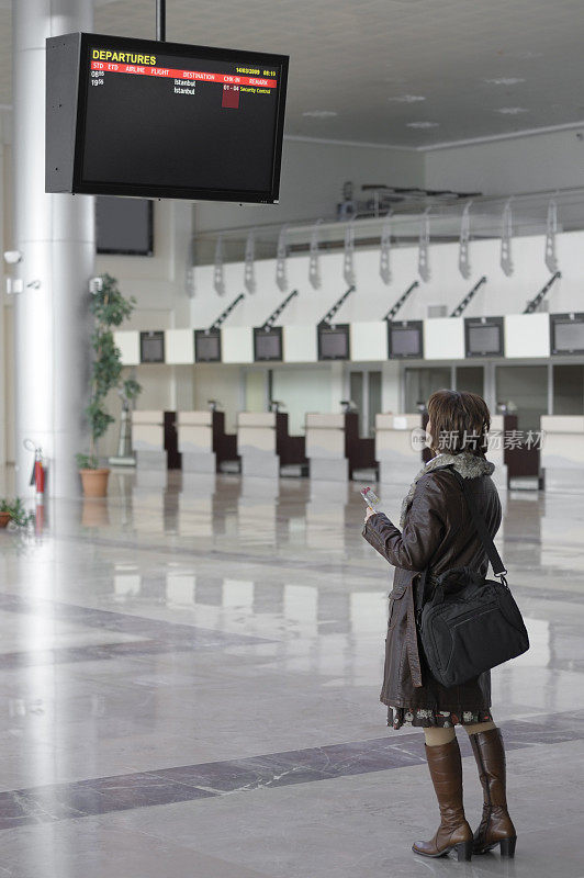 一个女人拿着机票，在机场看离港屏幕