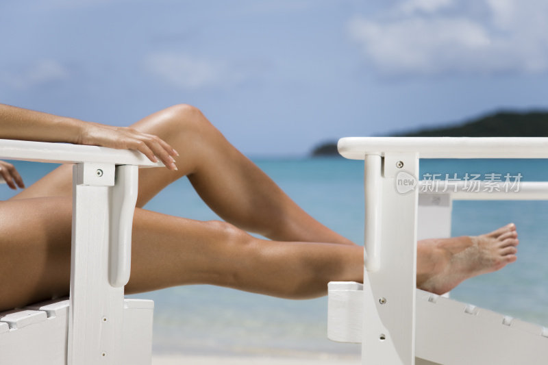 晒黑的女人的腿和白色沙滩椅