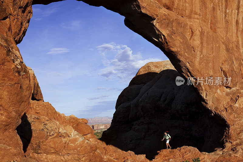在犹他州摩押的天然拱门下的危险岩石上的徒步者