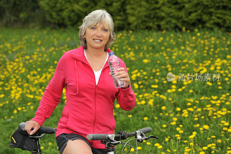 微笑的女人骑自行车和喝水。