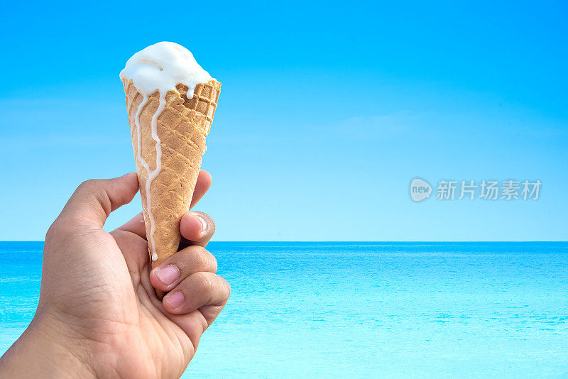 手握冰淇淋蛋卷背景是大海和蓝天。
