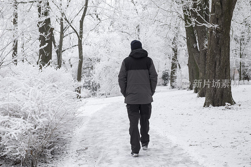 一个孤独的男人走在一条小路上，穿过城市公园里冰冻的冬季景观