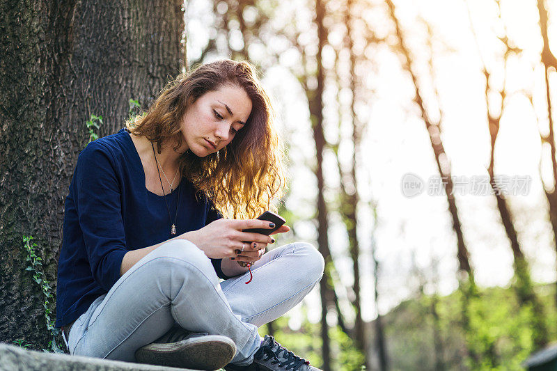 一个少女在公园里用手机发短信。