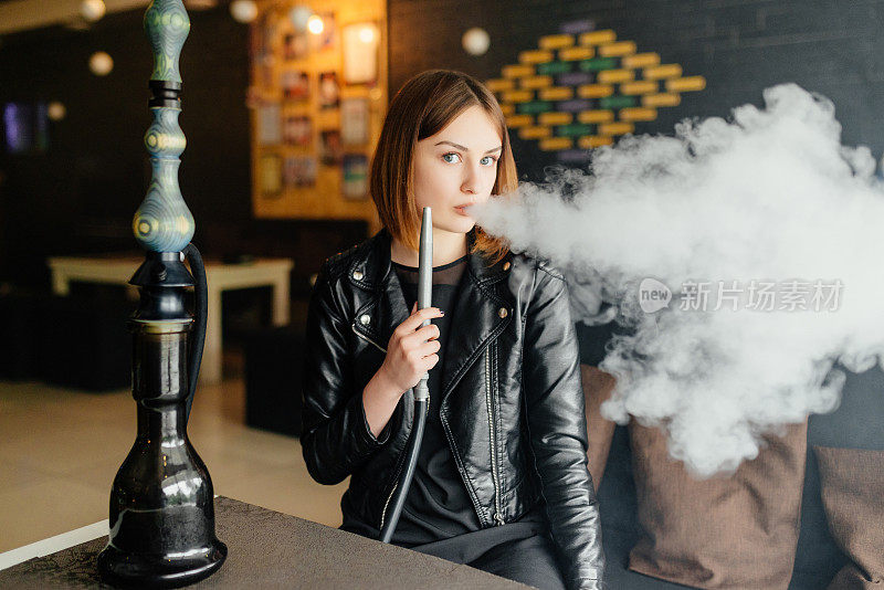 一个漂亮的年轻女孩在辛苦工作一天后休息，在咖啡馆抽水烟