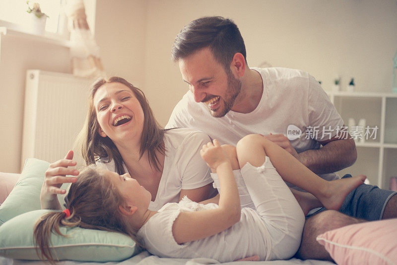 父母和他们的小女儿在床上玩得很开心。早上的家庭时光。