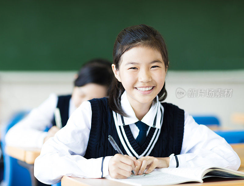 微笑的学生女孩在教室和她的朋友在后面