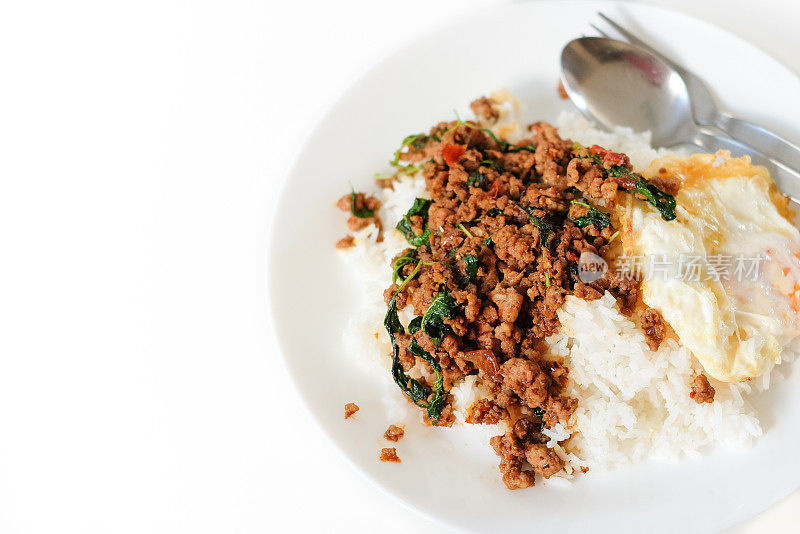米饭配上炒猪肉和罗勒叶，再配上煎蛋，放在白色的盘子里，配上勺子和叉子，这是泰国美食的流行理念。