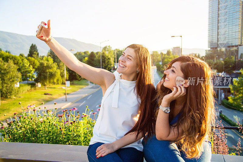 两个年轻的成年女子坐在桥上自拍