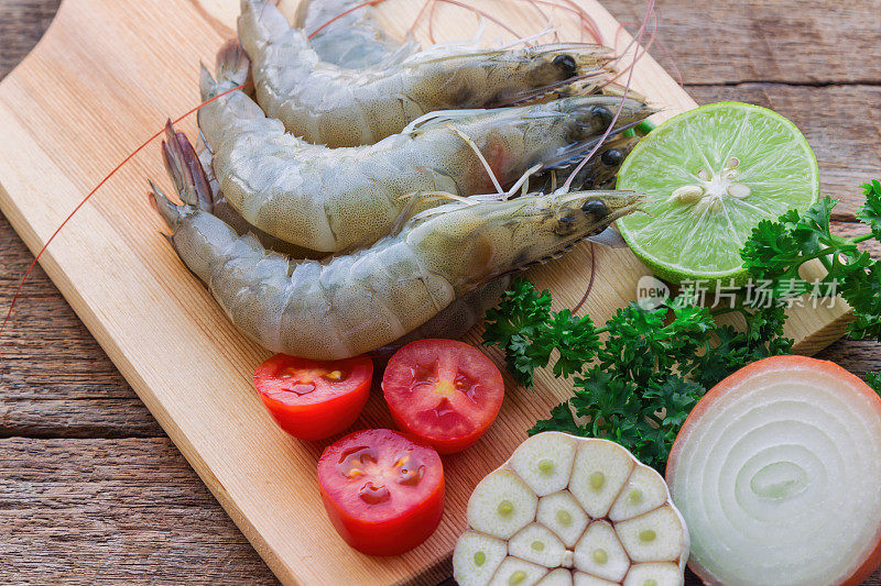 在近距离观察新鲜的白色虾木切板。在木桌上为海鲜菜单准备生虾、蔬菜和香草。自制美味食物的概念。