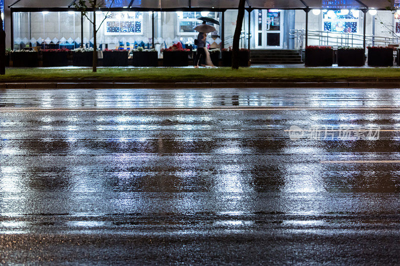 人们在雨夜走在人行道上。模糊的形象。