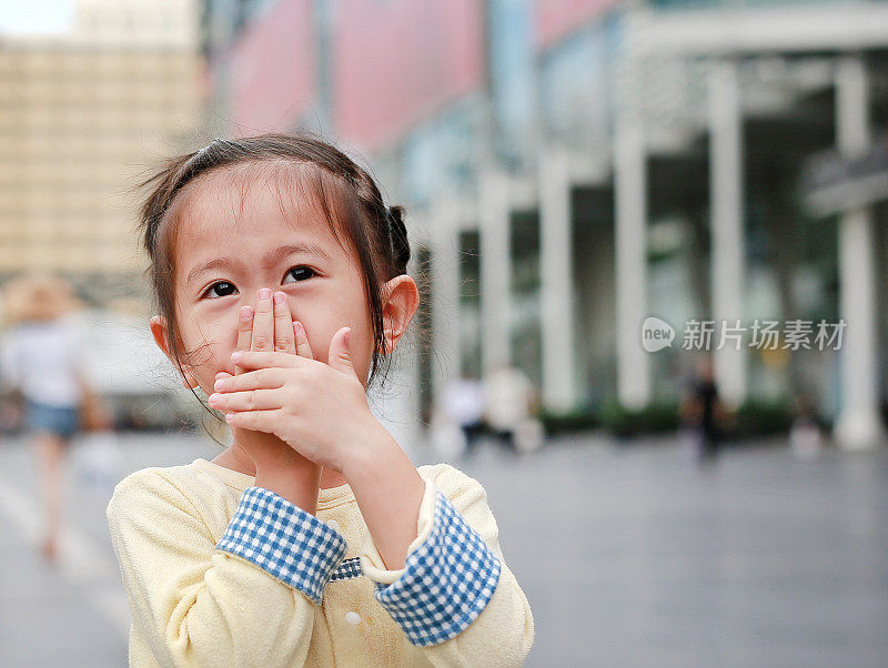 一个亚洲小女孩用手捂住自己的嘴和鼻子。