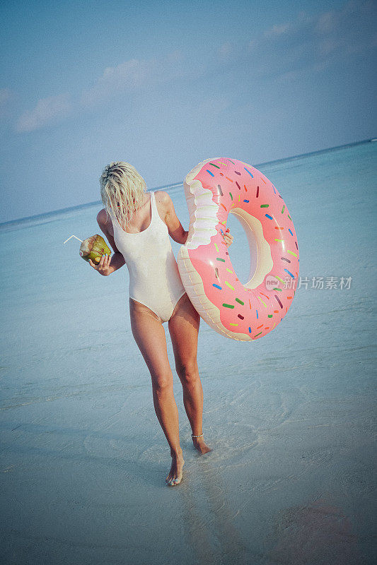金发女子站在马尔代夫的海边喝椰子水