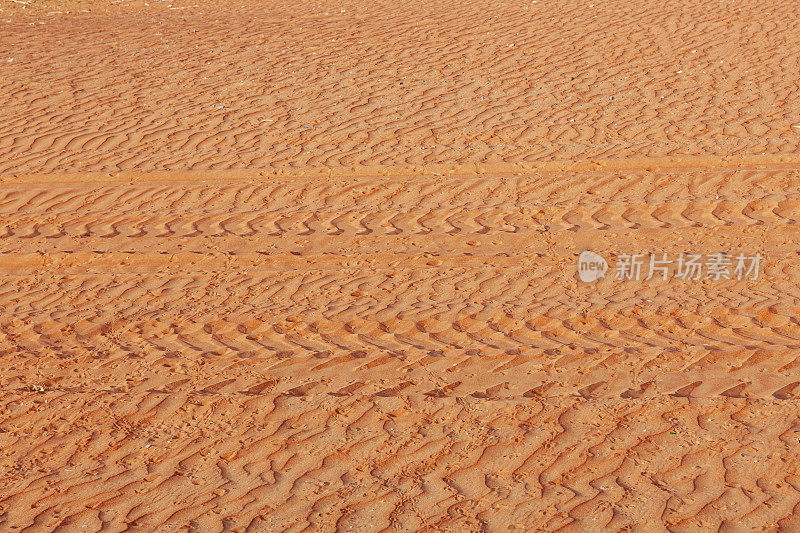 在阿拉伯联合酋长国迪拜城外的沙漠中，傍晚的阳光下，风在沙地上留下的SUV轮胎痕迹和图案;只有沙子，没有人。