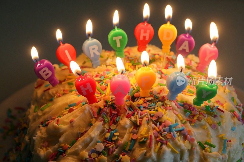 家庭制作的生日蛋糕的形象与多色点燃蜡烛拼写生日快乐，庆祝蛋糕覆盖白色奶油和糖果糊，照亮蜡烛火焰