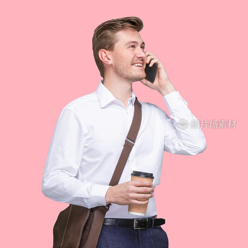 白人年轻男性经理站在有色背景前，戴着邮差包，拿着包，使用手机