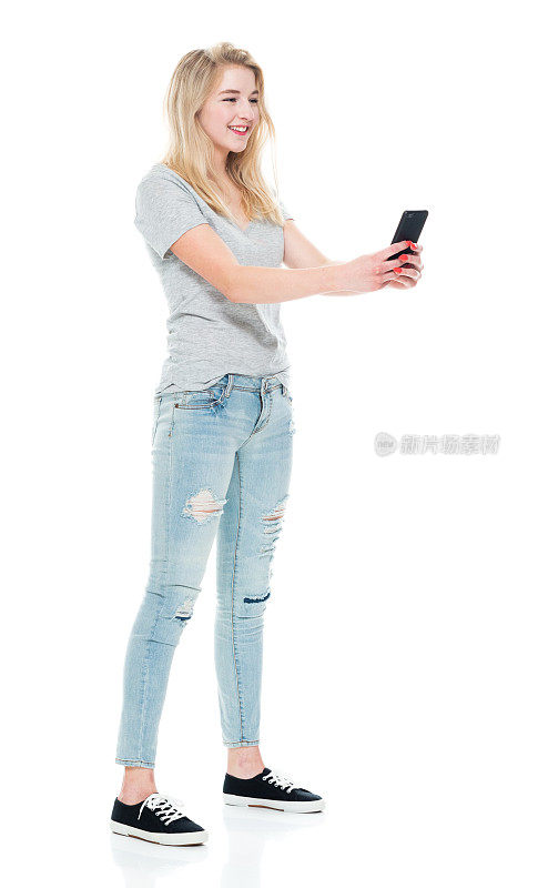 z一代的少女穿着牛仔裤站在白色背景前玩手机
