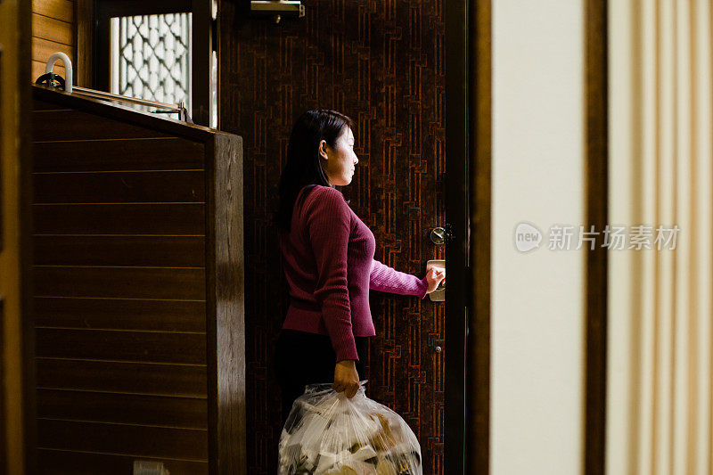 一张亚洲女人拿着垃圾袋离开房子的照片