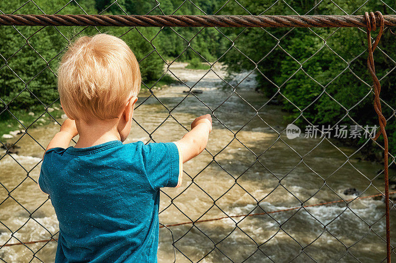 小男孩站在吊桥上，看着崎岖的山河