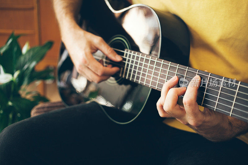 一个年轻人在家里弹吉他，试图打破压力重重的障碍，沉浸在音乐中。