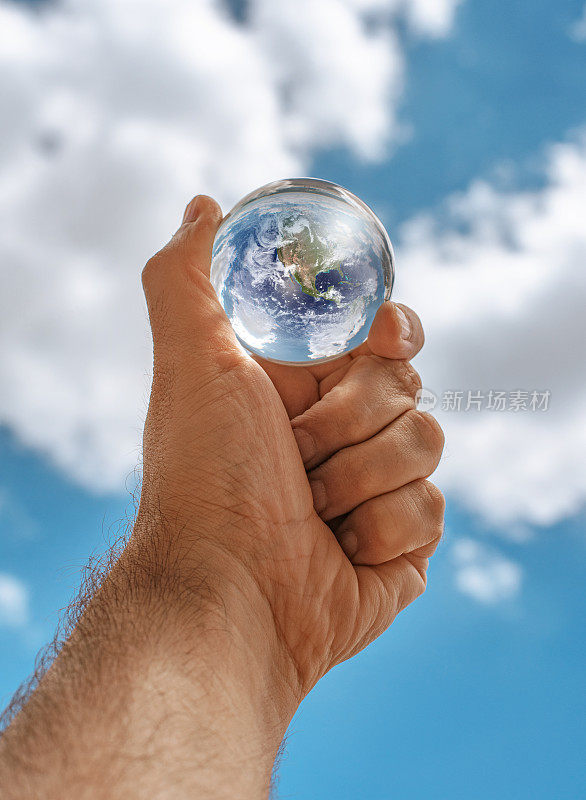 水晶球反映地球在人的手在一个蓝色的天空背景