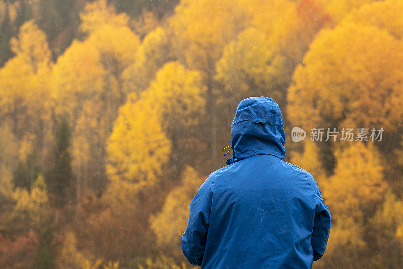 在秋天，一个穿着蓝色雨衣、看向别处的不可辨认的男人。