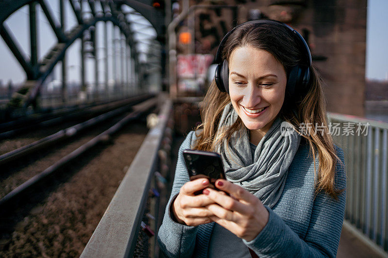 一个戴着耳机和智能手机的女人站在铁轨旁