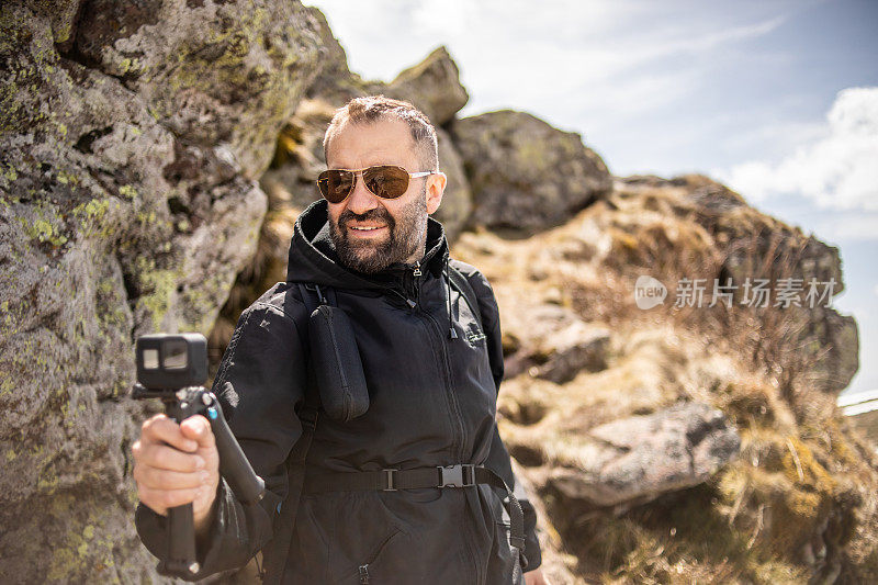 这名徒步者爬上山，用他的gopro相机拍摄，为他的视频博客制作视频。