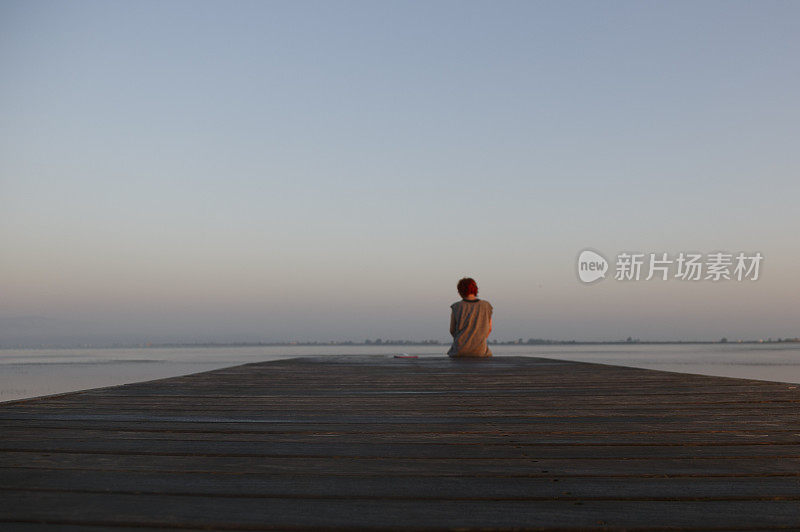 一个女人坐在木码头上望着大海