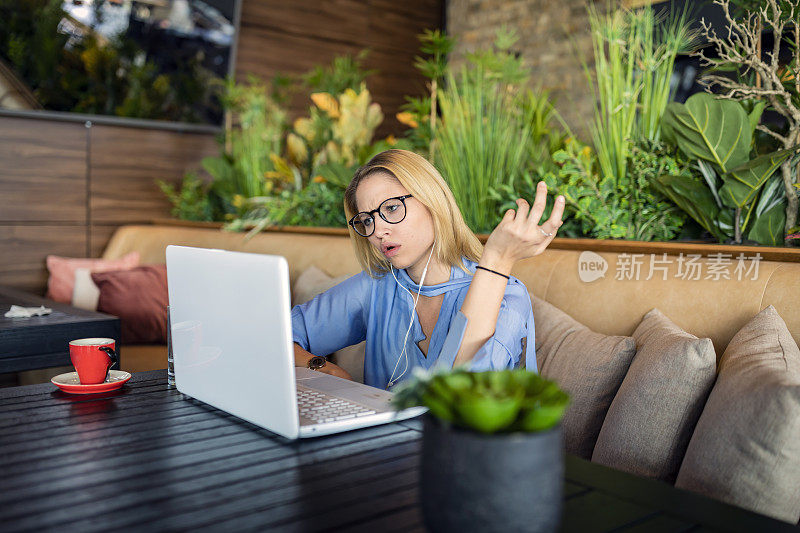 一个年轻迷人的女人正在用她的笔记本电脑，同时坐在现代的自助餐厅和她的朋友交流。