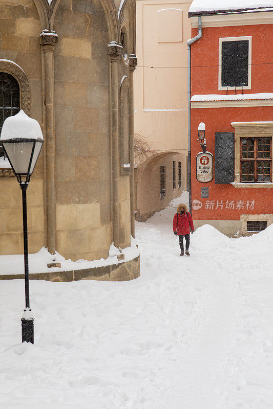 背着双肩包，穿着红色冬衣的男人走在被雪覆盖的城市街道上