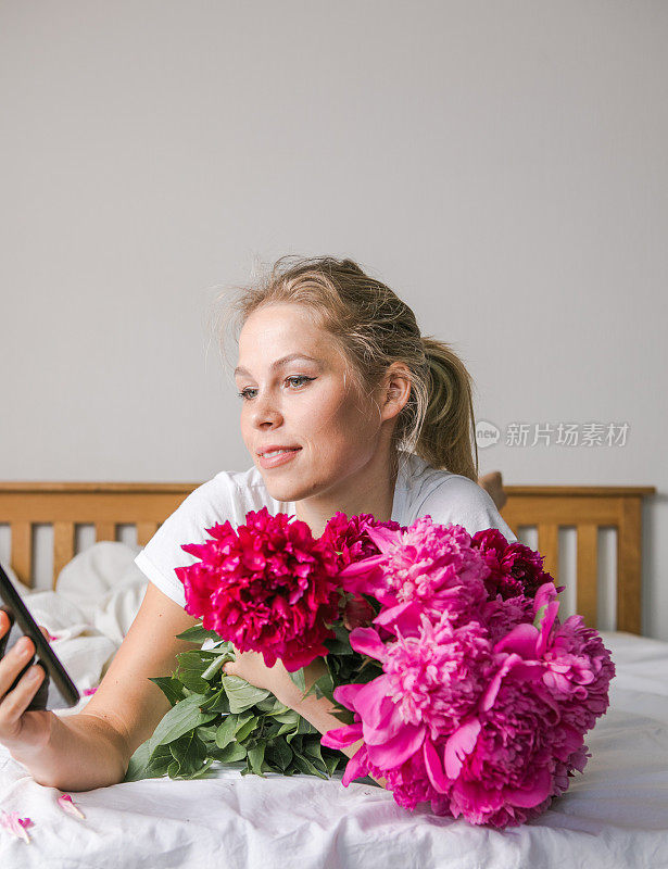 在线约会概念，在线社交概念。幸福的女人躺在床上，穿着睡衣，一边欣赏郁金香花，牡丹花束，一边打电话