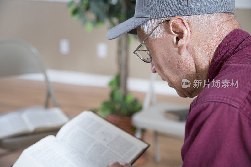 穿着随意的高级男士在会议室里等着其他人来参加圣经学习。他正在研读《圣经》。