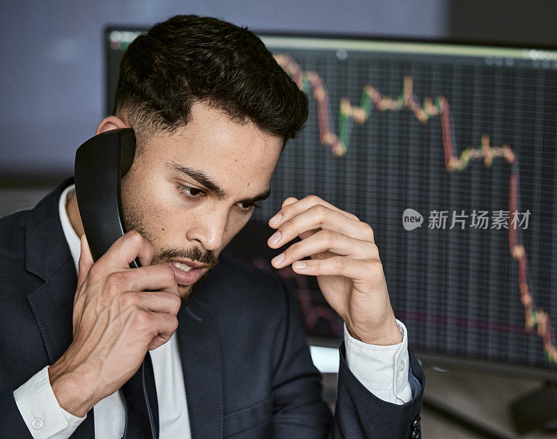 照片中，一个年轻的商人为了监控股票市场正在打电话