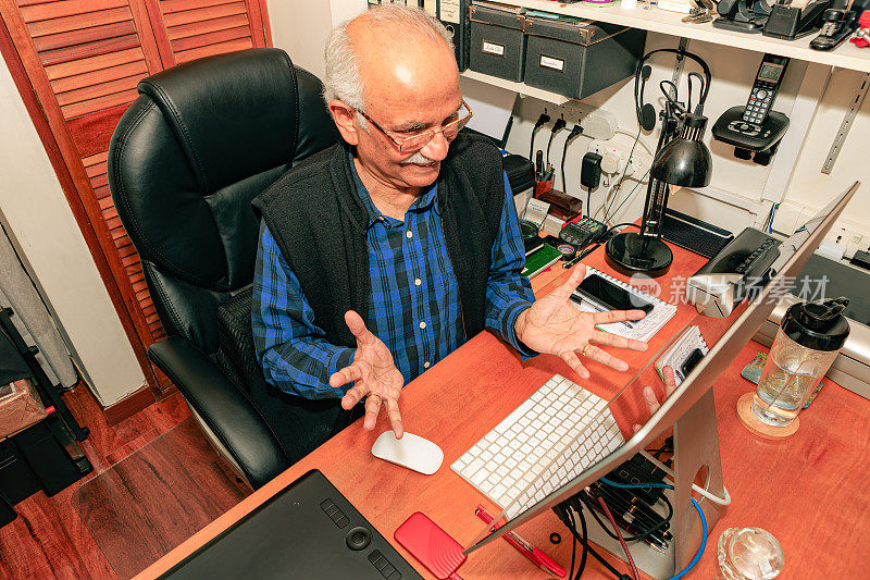 Bogotá，哥伦比亚-一个白发苍苍，74岁的亚洲印度人在他的家庭办公室在他的桌面电脑上工作。他的手好像在说:“完成了，而且完成得很好。”