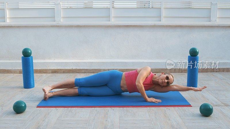 健身妇女躺在侧手在平板的位置，另一只手伸展在运动垫上