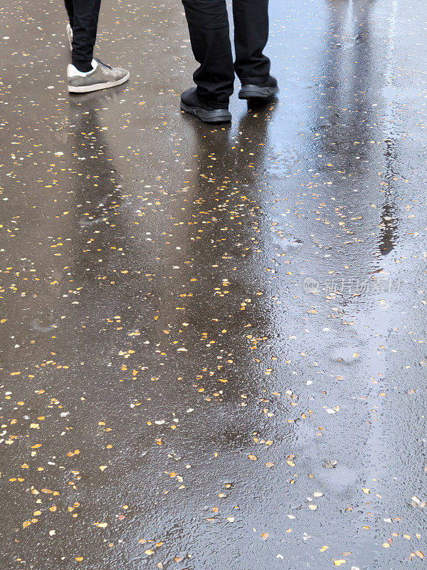 两个穿着白色运动鞋和蓝色运动裤的男人走在潮湿的人行道上。