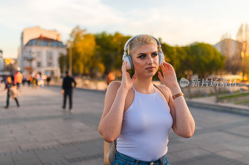 美丽的年轻女子，金色短发，一边听音乐，一边穿过城市