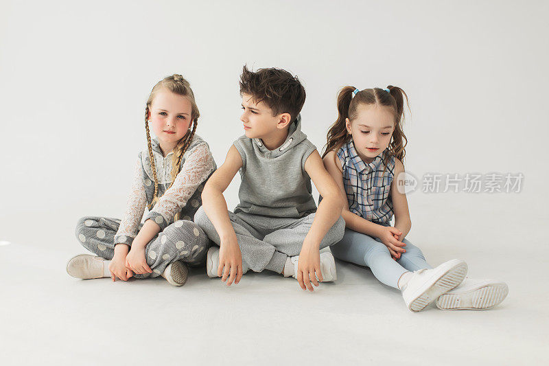 两个穿着浅色衣服的女孩和男孩坐在摄影棚的白色背景上。宝宝的牙齿。快乐的童年。幼儿园的年龄。开朗的孩子。顽皮的女孩。中东的男孩