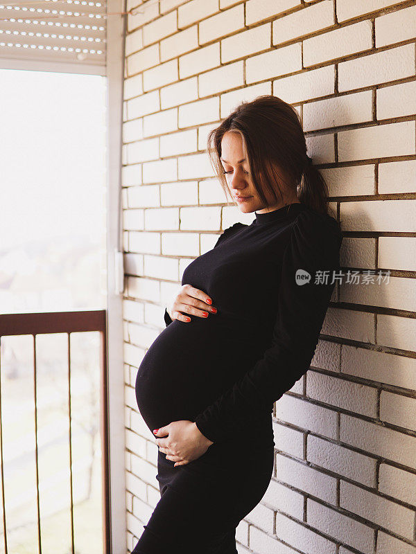 一个孕妇站在窗边，抱着肚子