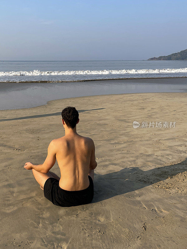 特写图像的裸胸印度印度男子练习莲花姿势(莲花)瑜伽位置湿沙滩，水的边缘，重点在前景，后视图