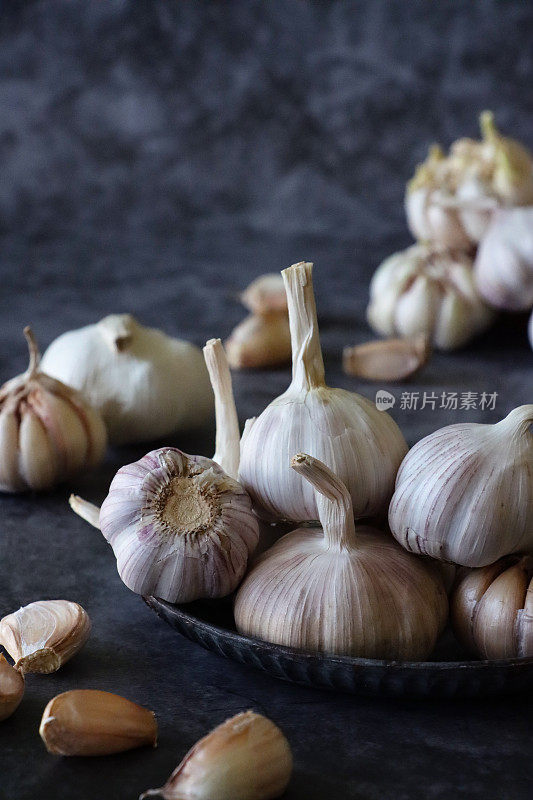 特写图像堆大蒜鳞茎在斑驳的黑色盘子周围的丁香，斑驳的黑色背景，重点在前景，复制空间