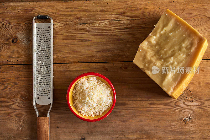 磨碎的奶酪在碗里，有块和磨碎器，放在木桌上