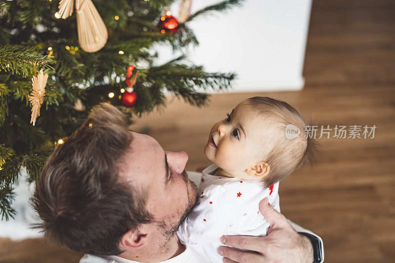 微笑的女婴看着圣诞树，而他的父亲的怀里