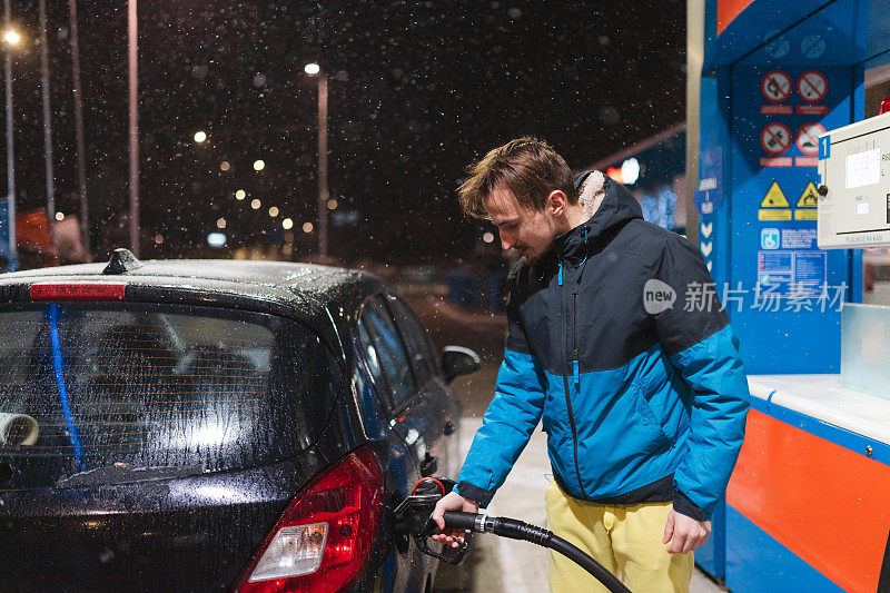 年轻男子晚上在加油站给汽车加油