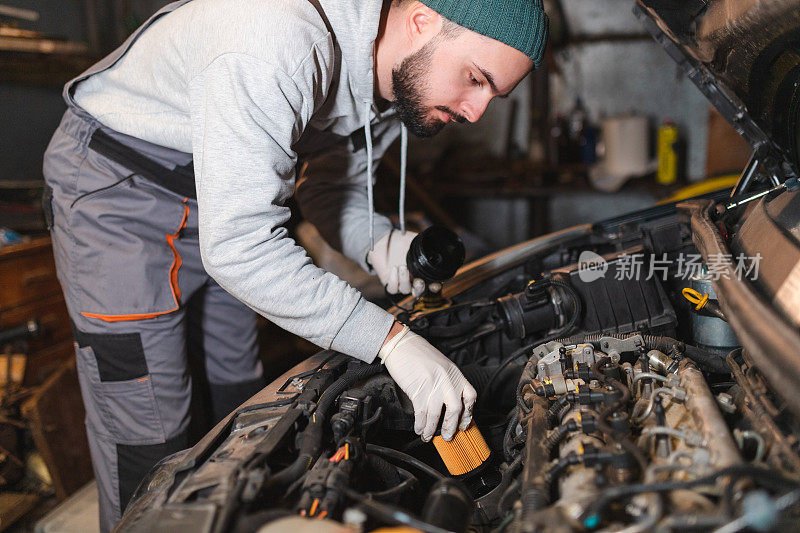 年轻的机械师正在他的车库里给一辆汽车安装新的机油过滤器