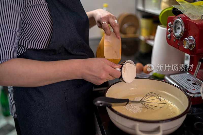 女厨师将一杯面粉倒入搅拌碗中。烘焙饼干的概念