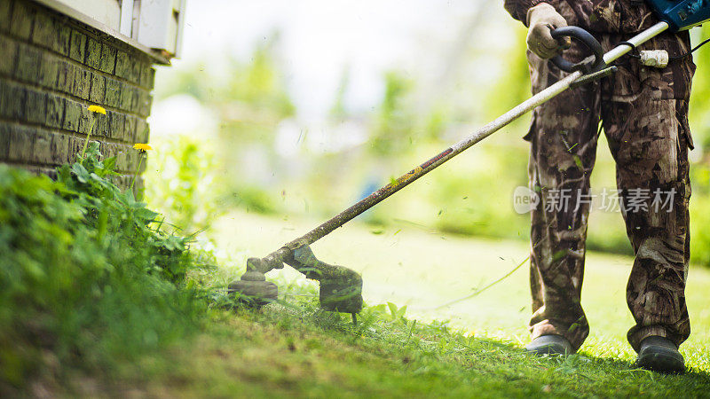 男子在后院用电动或汽油草坪修剪机修剪高草。园艺护理工具和设备。用手动割草机修剪草坪的过程