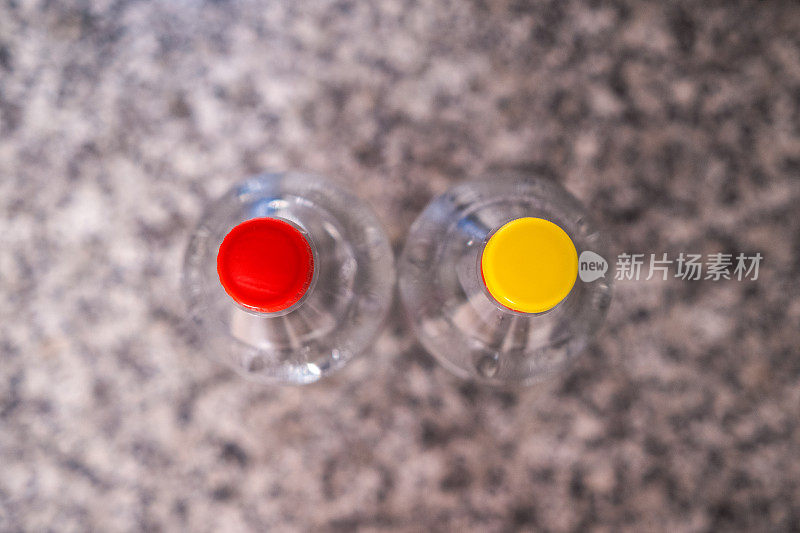 厨房长凳上的两个塑料瓶，突出了它们的红色和黄色瓶盖。