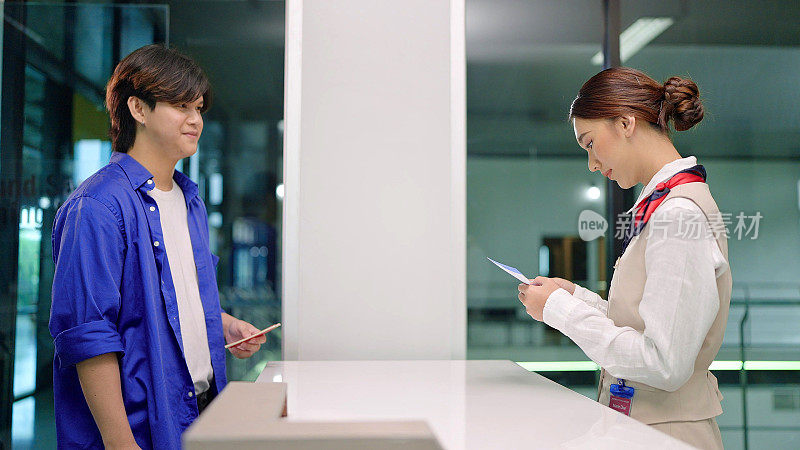 年轻的亚洲女地勤人员在机场的航空公司柜台前检查旅客的登机牌和机票。飞机旅行和运输