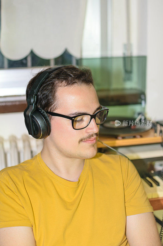 戴着眼镜的年轻人在房间里用老式耳机听着黑胶唱片